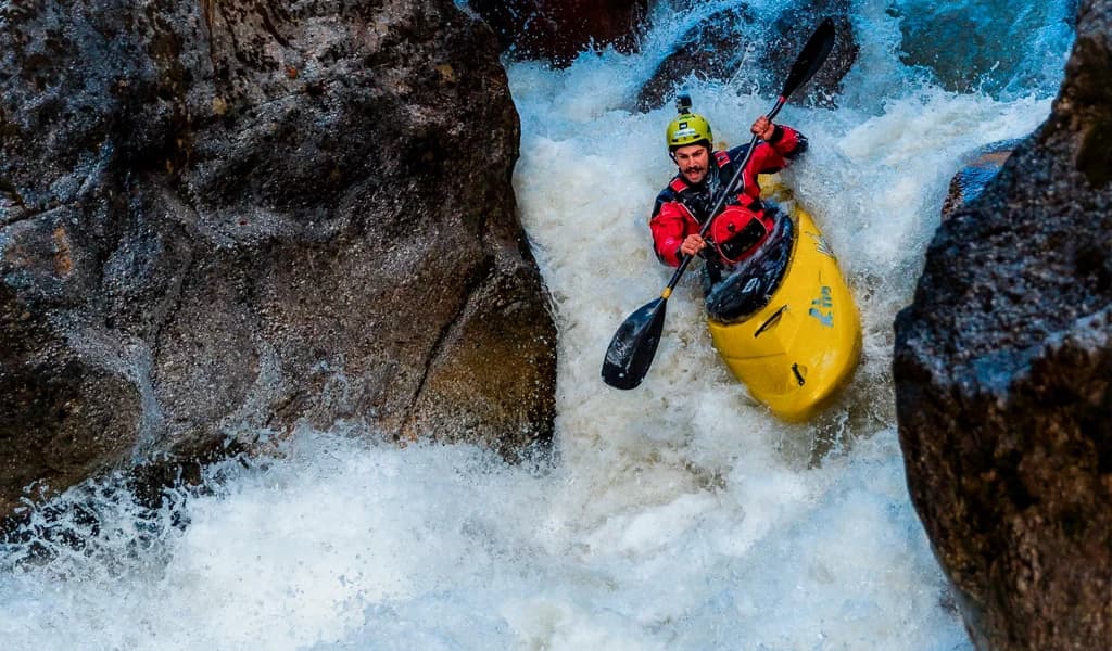 A kayaker paddles hard through churning whitewater between narrow canyon rocks.