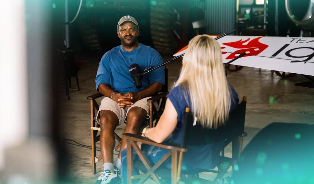 A seated interview between Selema Masekela and Emma McDonald, microphones between them, inside an aircraft hangar.