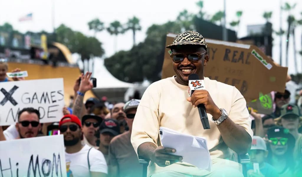 Selema Masekela holding a microphone and smiling while addressing a crowd at an outdoor sports event.