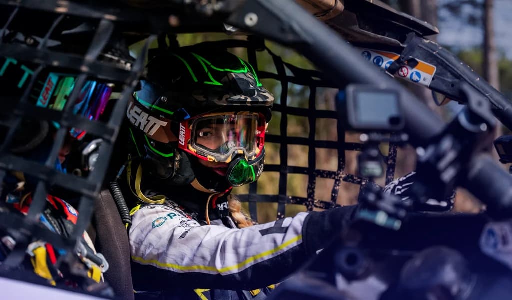Christine GZ driving an off-road vehicle wearing a helmet and safety gear.