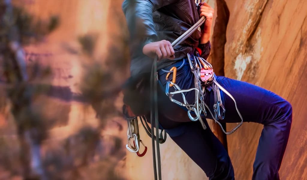 Close-up of JJ Yosh’s harness loaded with carabiners and gear on a red sandstone wall.