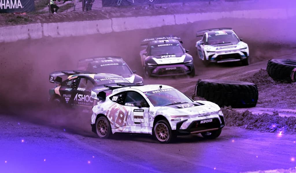 Rally cars speeding through a dirt track corner, kicking up dust during a competitive race.