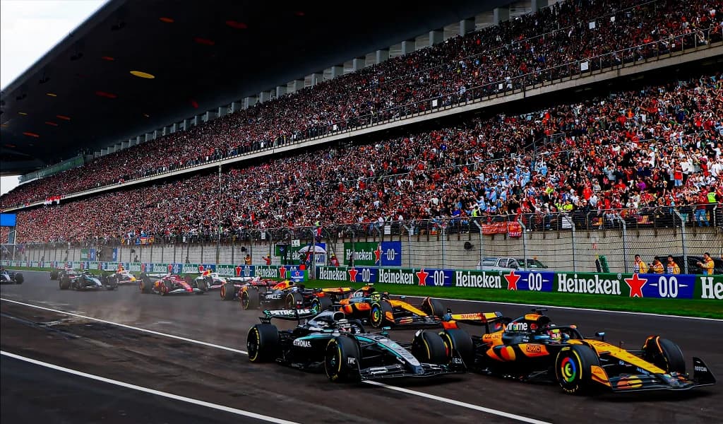 Formula 1 cars racing past a packed grandstand during a race.